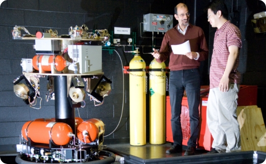 two researchers standing next to a large device in lab