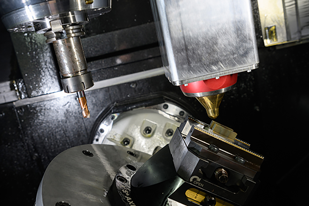Close-up of advanced manufacturing equipment with a CNC machine tool and a laser or additive manufacturing nozzle positioned over a metal workpiece.