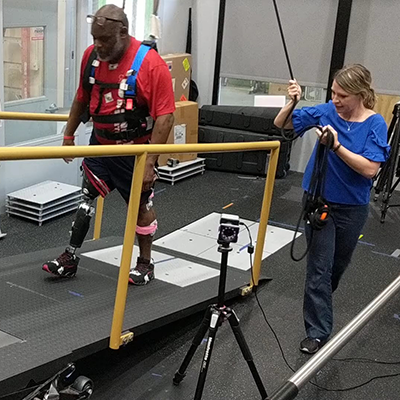 female researcher holding a cable while assisting  on a male test subject wearing an exoskelton device and walking on an incline ramp