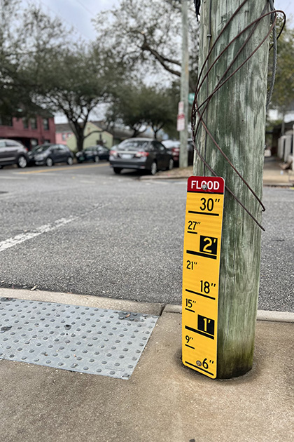 a yellow sign marking flood levels with inch marks leans against bottom of electric pole on the corner of a street 
