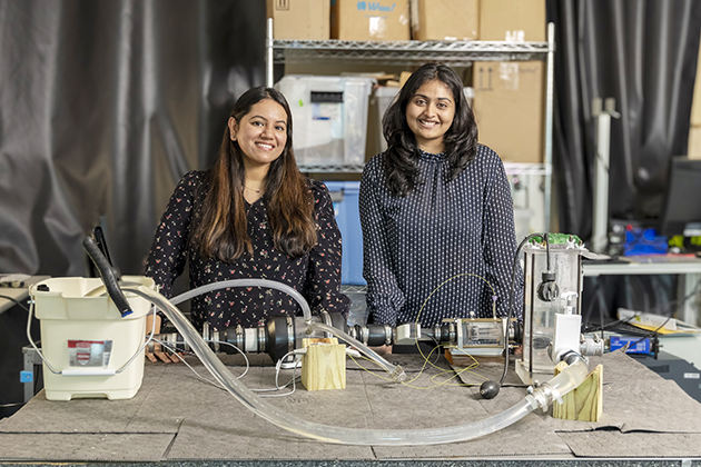 Two female researchers stand in a lab behind a device that prints 3D heart valves.