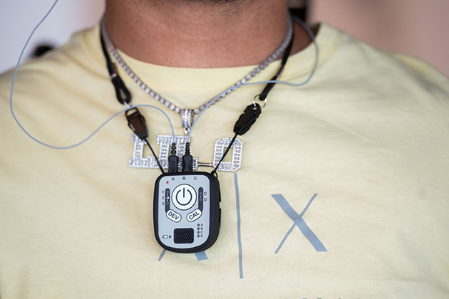Close-up of a chest-worn assistive electronic device connected by wires to adhesive sensors on the upper chest, used for monitoring or control.