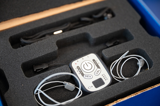 Assistive device with cables and electrodes packaged in a foam case, showing components used for setup and transport.