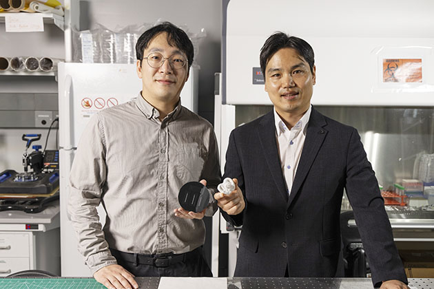 Two male researchers standing in a Georgia Tech lab with one holding a new pacifier under development.