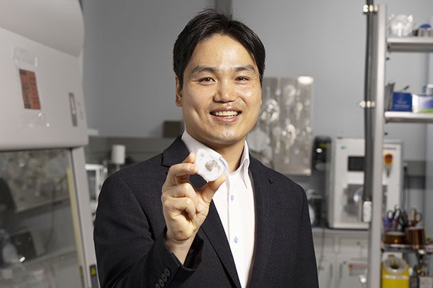 Male researcher wearing a black suit holds a pacifier while standing in a lab at Georgia Tech.