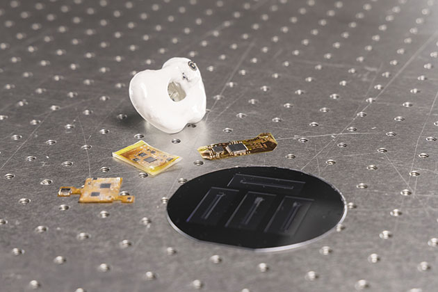 A white pacifier on a metal table next to several electronic chips