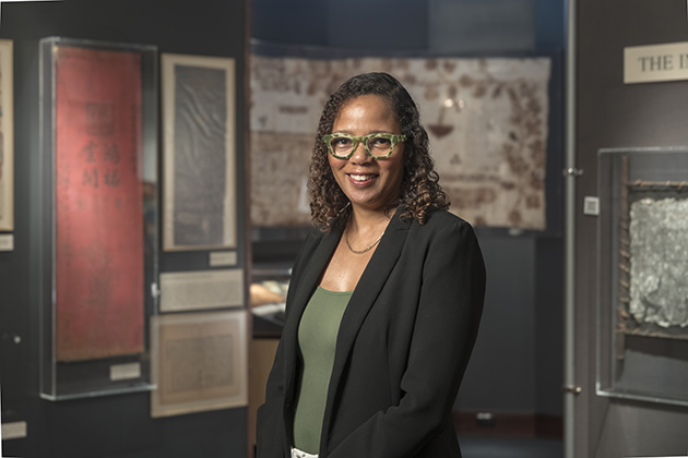 female standing and wearing green glasses, a green shirt, and a black suit jacket