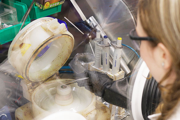 A female researcher in a lab removing a silicon solar chip prototype from a device with vapors swirling around.