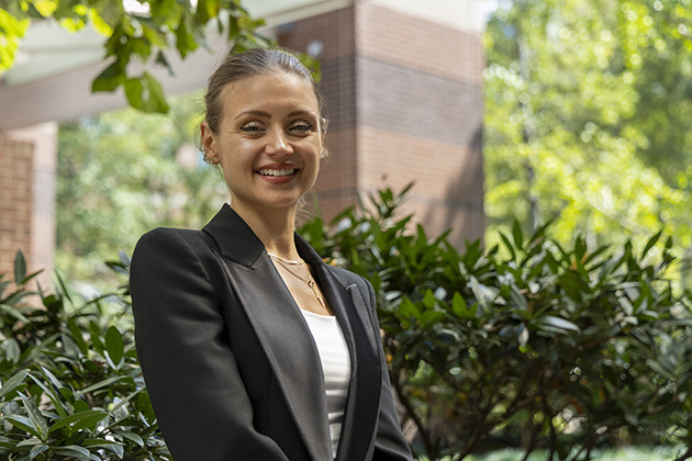 female with her hair pulled up and wearing a black suit jacket standing in front of foliage