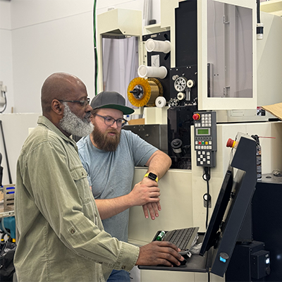 two men standing in front of a beige industrial piece of equipment