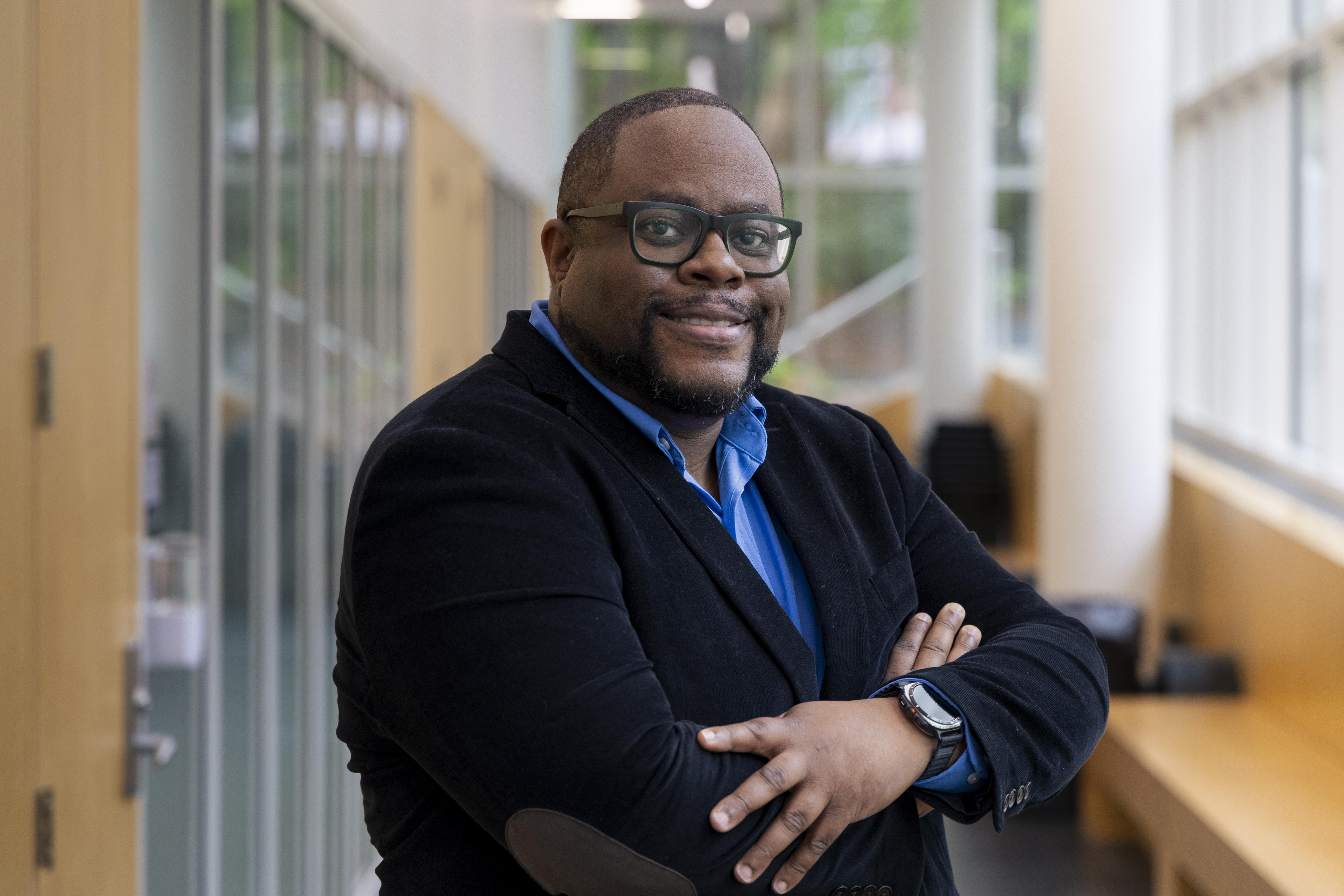 /Man%20with%20crossed%20arms%20standing%20in%20a%20hallway%20with%20many%20windows