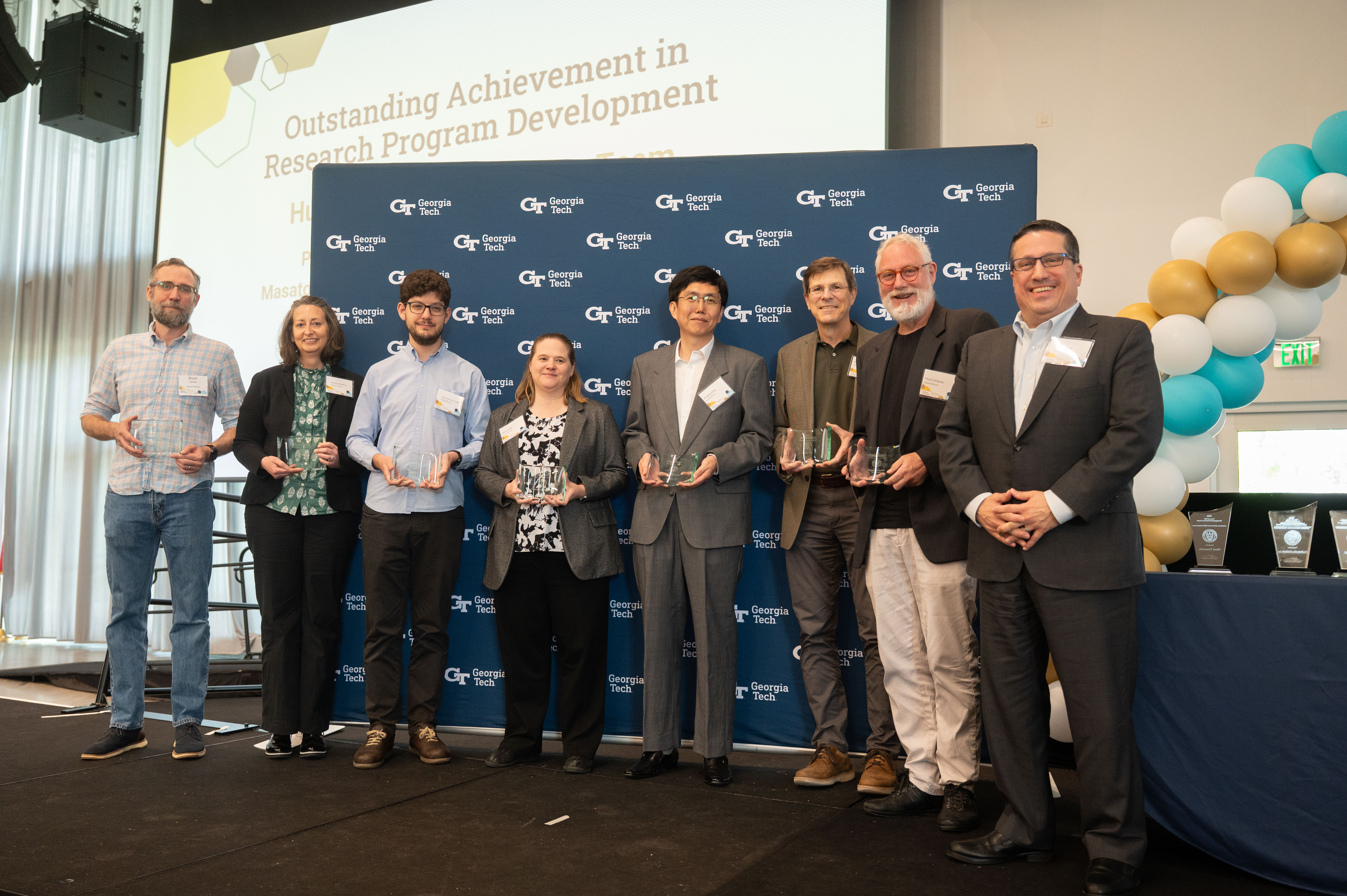 The Human Space Exploration research team smiles in front of a Georgia Tech background holding their awards on stage.