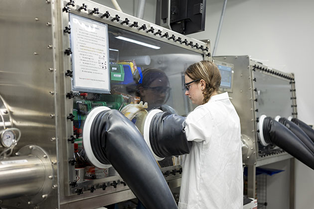 female researcher in white lab coat using a laboratory glove box