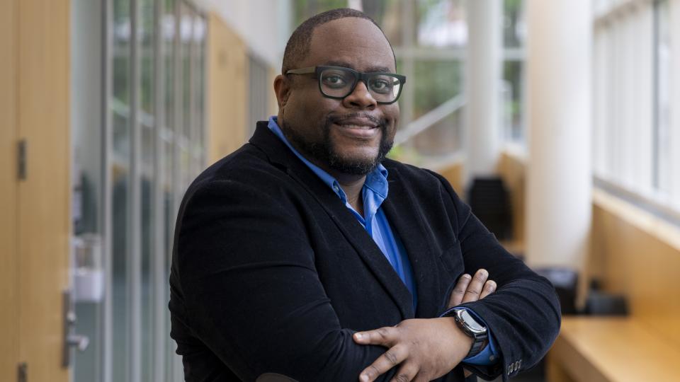 Man with crossed arms standing in a hallway with many windows
