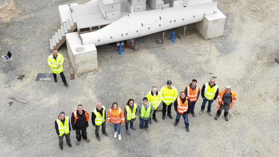 Aerial shot showing members of the Re-Wind Network stand in front of a pedestrian bridge made using decommissioned wind turbine blades