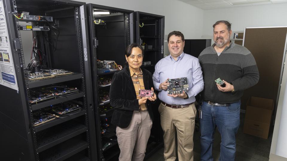 Three researchers stand in front of a rack of computing equipment.