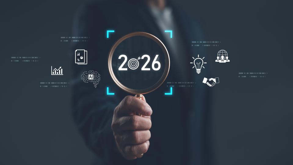 Businessman holding magnifying glass focusing on year 2026 with digital icons of innovation, AI, analytics, and global strategy. Concept of future planning, technology trends and vision. 