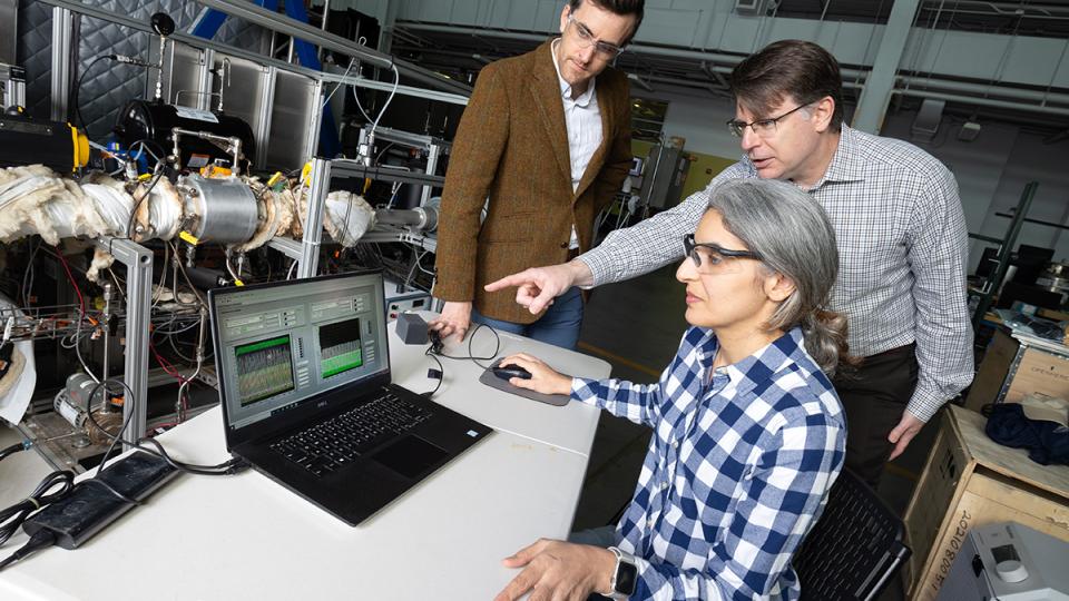 Postdoctoral fellow Poorandokht Kashkouli, seated at laptop, discusses test data from their direct air capture rig. Ryan Lively, left, and Chris Jones, pointing at laptop, stand next to the rig, which is a series of tubes and valves in a metal frame. (Photo: Candler Hobbs)
