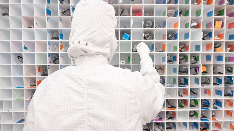 Person in cleanroom gear selecting glasses