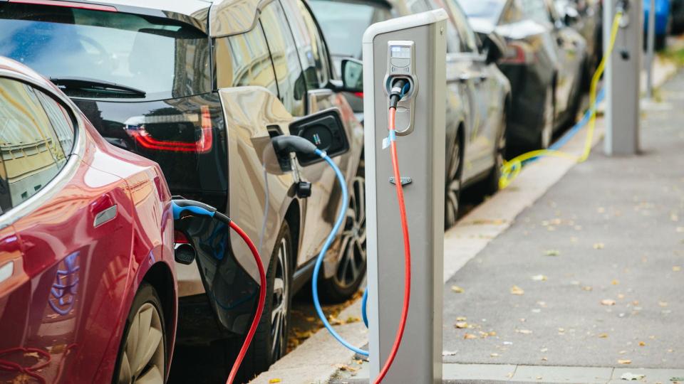Row of electric vehicles parked on a street and charging from charging poles