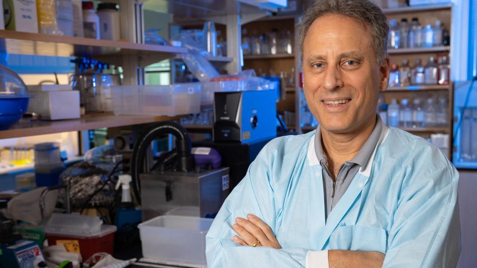 Mark Prausnitz poses with arms crossed in his lab with shelves of materials and bottles in the background.
