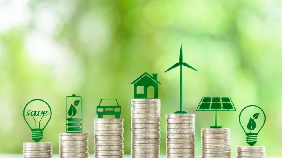 Stacks of coins topped with green icons representing clean energy and sustainability.