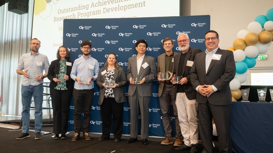 The Human Space Exploration research team smiles in front of a Georgia Tech background holding their awards on stage.