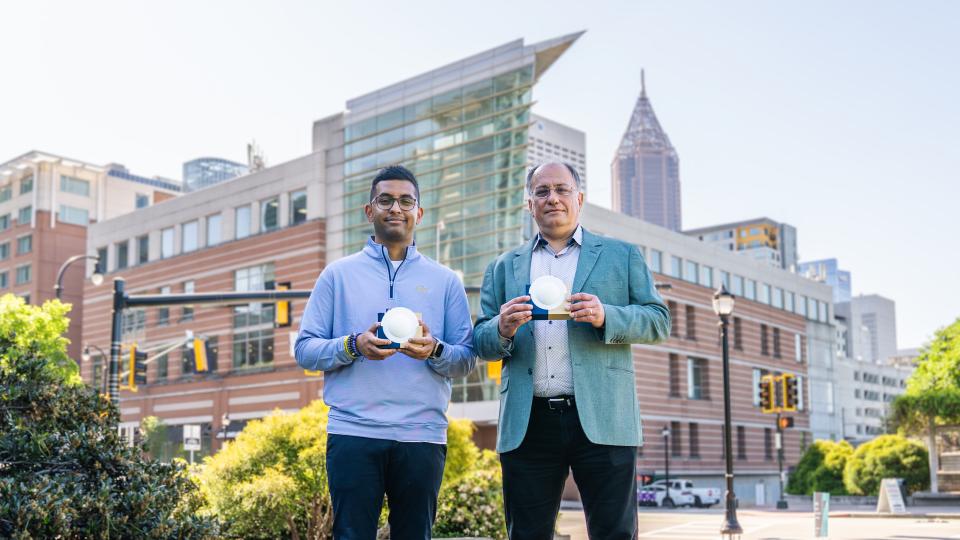 Professor Emmanouil “Manos” Tentzeris and Ph.D. student Marvin Joshi hold a lens‑enabled backscatter system that could support battery‑free wireless communication across future smart city infrastructure.