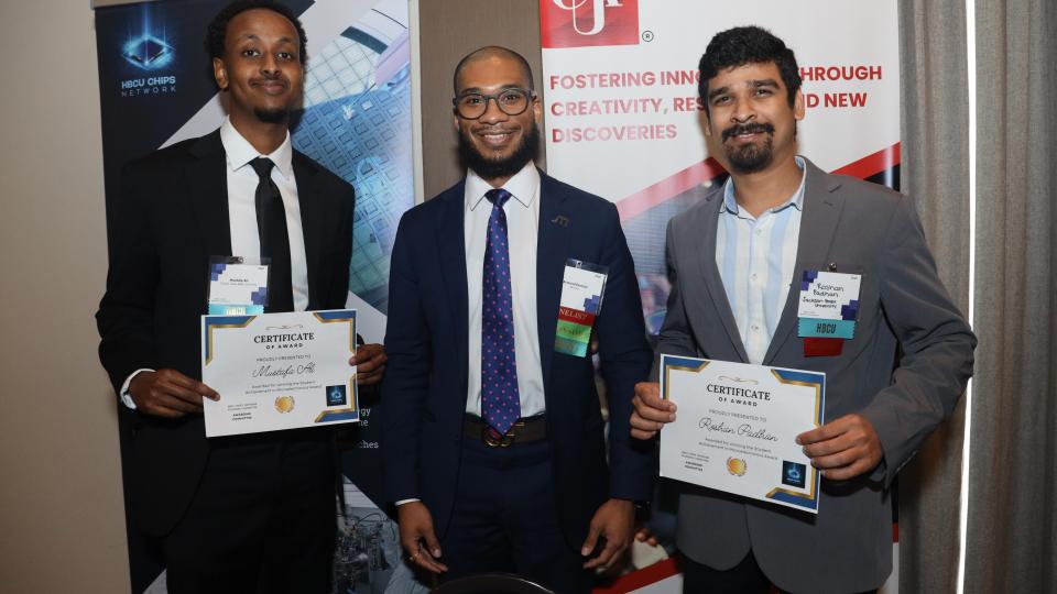 Three men in business attire stand side by side at a professional event, smiling at the camera. The men on the left and right hold certificates of award. Behind them are banners for the HBCU Chips Network and Clark Atlanta University’s Research and Sponsored Programs, highlighting innovation, creativity, and research.