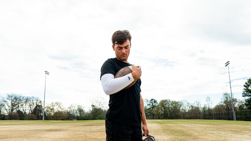 Football player holding a football while wearing a white VETTEX performance arm sleeve on an outdoor field.