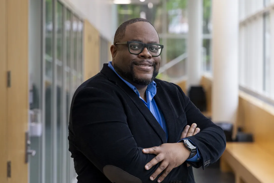 Man with crossed arms standing in a hallway with many windows