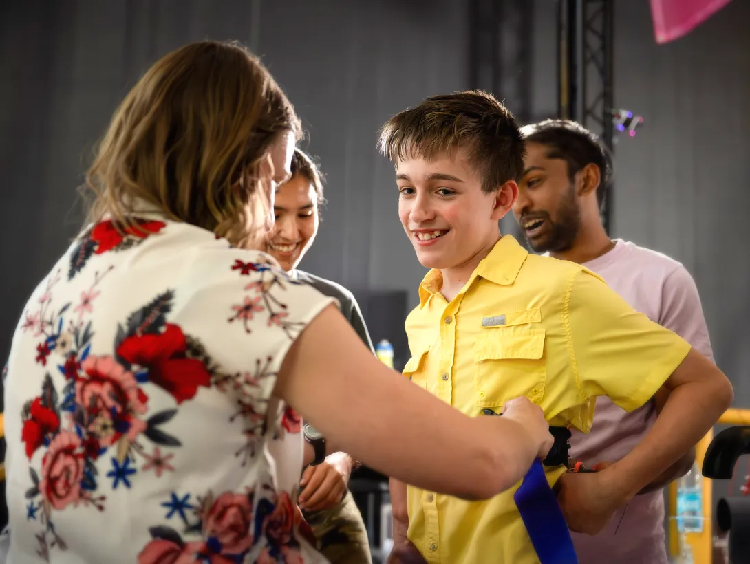 Person wearing a floral-patterned shirt interacting with a group of people indoors; one individual is dressed in a bright yellow button-up shirt.