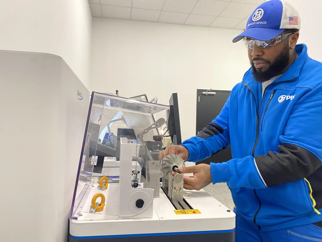 This is a photo of a technician at PBS Aeros space placing a part on a balancing machine in the company's manufacturing facility