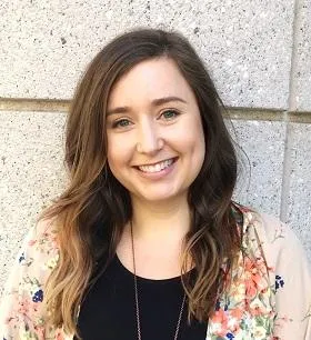 A smiling woman with long brown hair, wearing a black t-shirt and a floral cardigan