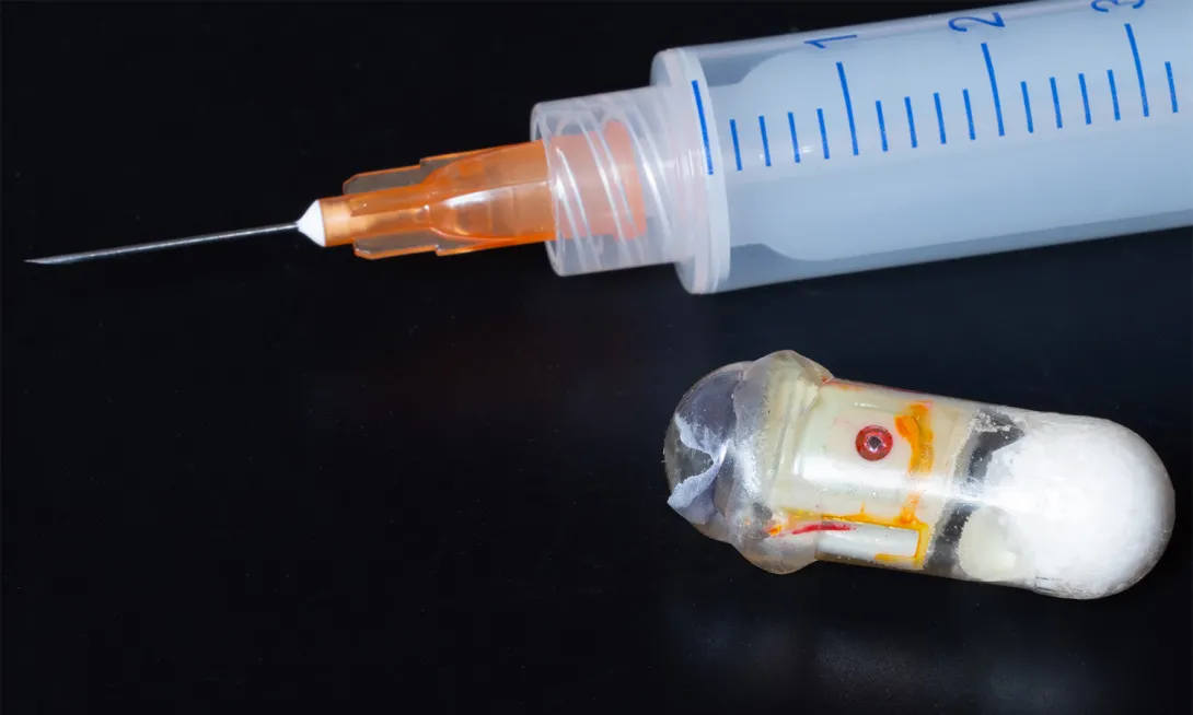 Prototype of an "exploding" capsule next to a syringe. The capsule can deliver medications that are typically only effective if injected.