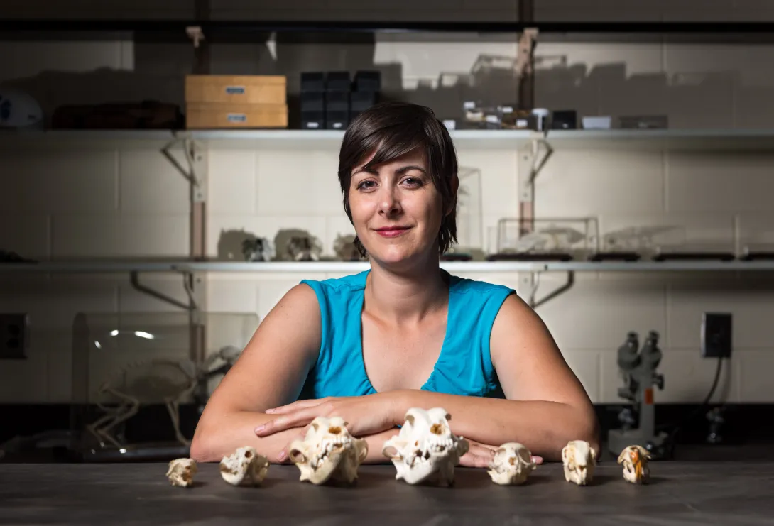 A woman stands behind a row of skulls.