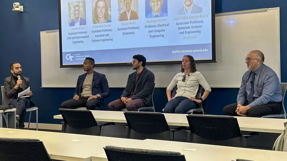 Five panelists sit at the front of a classroom during a Georgia Tech event, with one person speaking into a microphone. A projected slide behind them displays speaker headshots and names from the Institute for Matter and Systems.